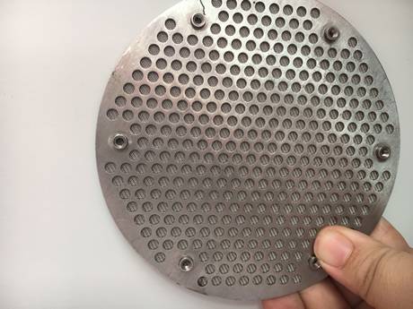 Una mano está llevando a cabo una forma redonda perforó el disco sinterizado metal del filtro.